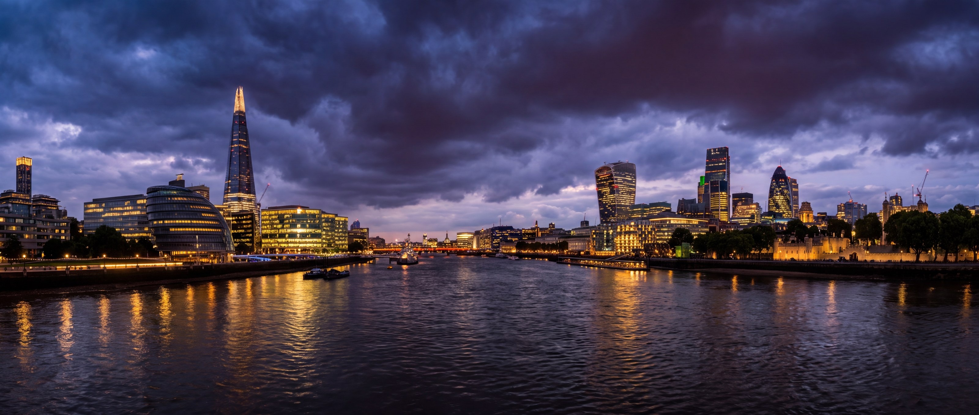 The London skyline at dusk across the Thames, the Shard and the City lit against storm clouds